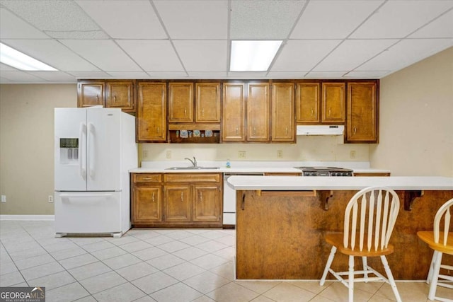 kitchen with a kitchen breakfast bar, a paneled ceiling, light tile patterned floors, sink, and white appliances