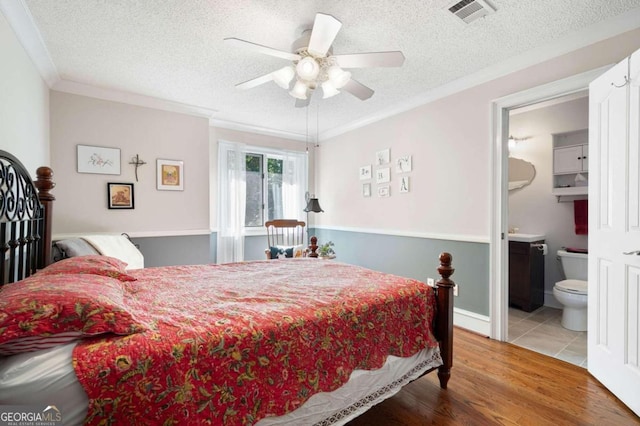 bedroom with light hardwood / wood-style floors, crown molding, connected bathroom, and ceiling fan