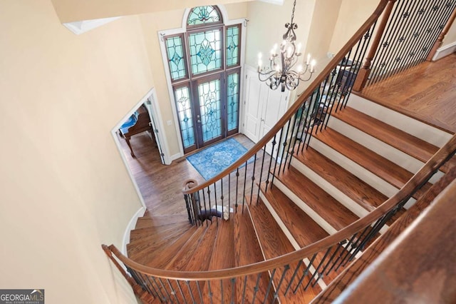 stairway with a high ceiling, a notable chandelier, and wood-type flooring