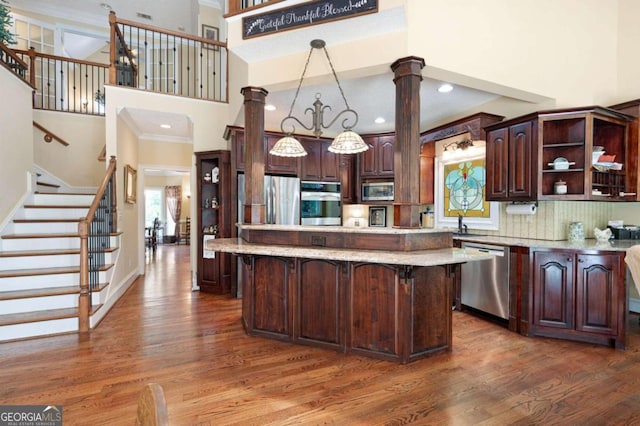 kitchen featuring appliances with stainless steel finishes, decorative backsplash, ornate columns, dark hardwood / wood-style flooring, and a kitchen island