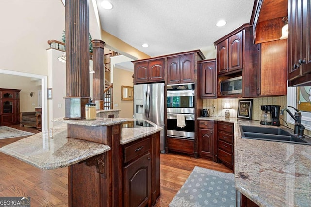 kitchen with sink, appliances with stainless steel finishes, light hardwood / wood-style flooring, decorative backsplash, and light stone countertops