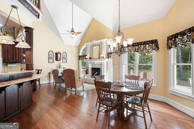 dining room featuring ceiling fan with notable chandelier, high vaulted ceiling, wood-type flooring, and a premium fireplace