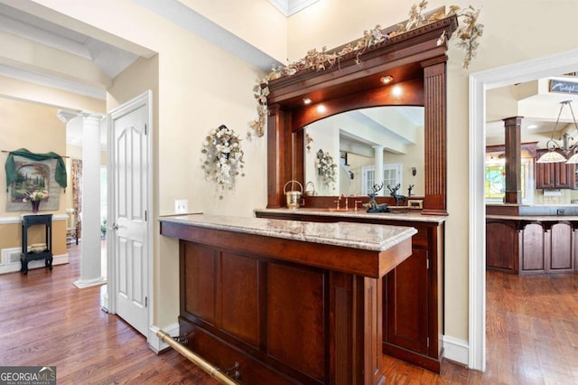 bar with light stone countertops, decorative columns, and dark hardwood / wood-style flooring