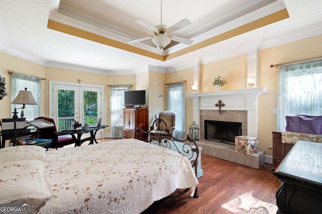 bedroom with a raised ceiling, dark wood-type flooring, ornamental molding, and a high end fireplace