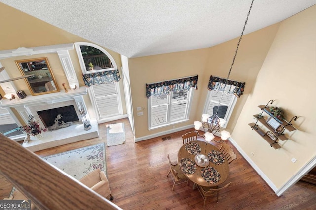 living room featuring high vaulted ceiling, wood-type flooring, a high end fireplace, and a textured ceiling