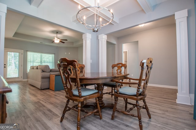 dining space featuring a raised ceiling, ceiling fan with notable chandelier, wood-type flooring, and ornate columns