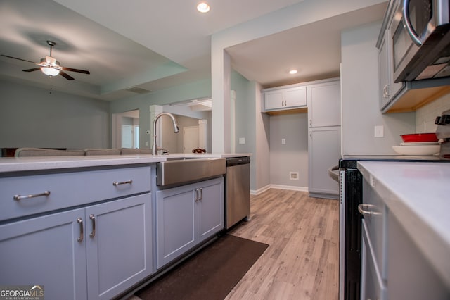 kitchen featuring stainless steel appliances, light hardwood / wood-style floors, gray cabinetry, a tray ceiling, and ceiling fan