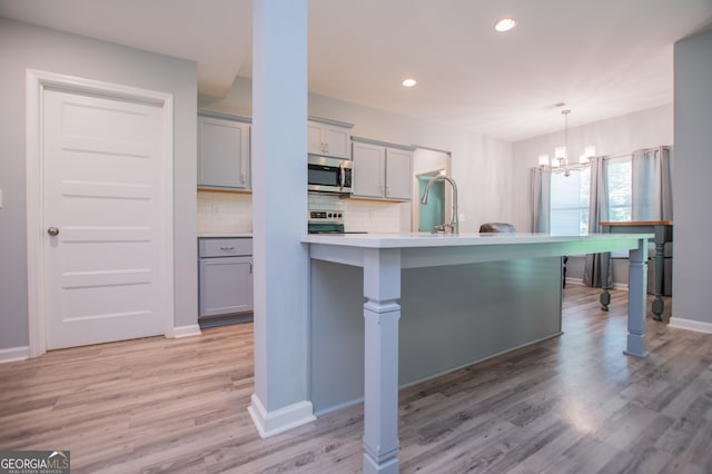 kitchen featuring decorative light fixtures, light hardwood / wood-style floors, decorative backsplash, gray cabinetry, and a notable chandelier