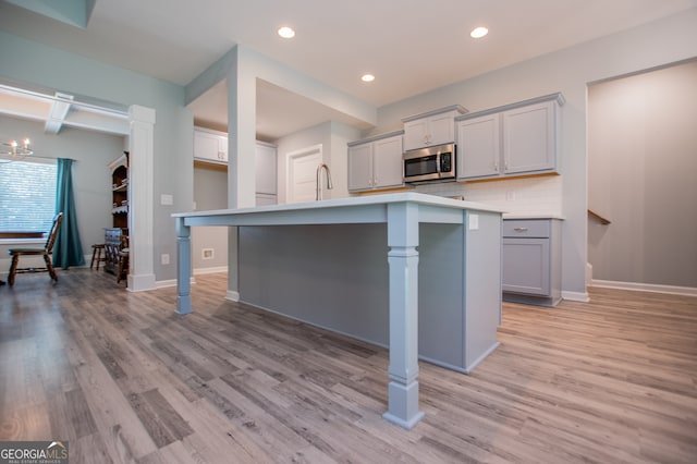 kitchen featuring light hardwood / wood-style flooring, a center island with sink, gray cabinets, and tasteful backsplash