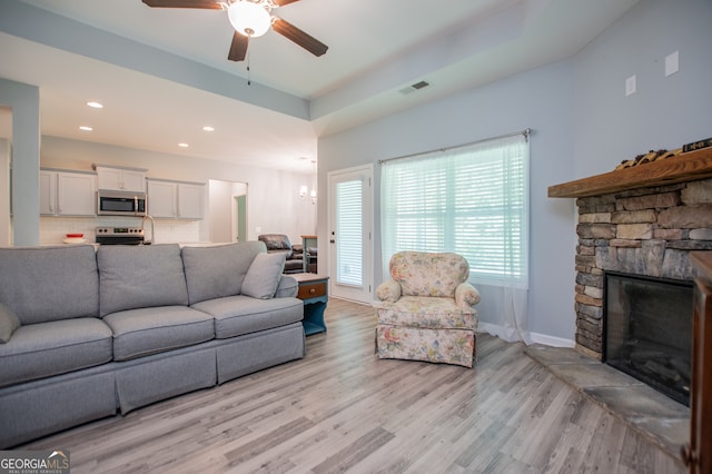 living room with ceiling fan, light wood-type flooring, and a stone fireplace