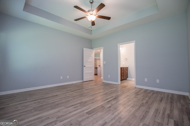 unfurnished bedroom with connected bathroom, a raised ceiling, and hardwood / wood-style flooring