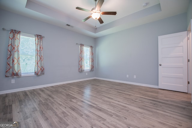 empty room with ceiling fan, a raised ceiling, and hardwood / wood-style floors