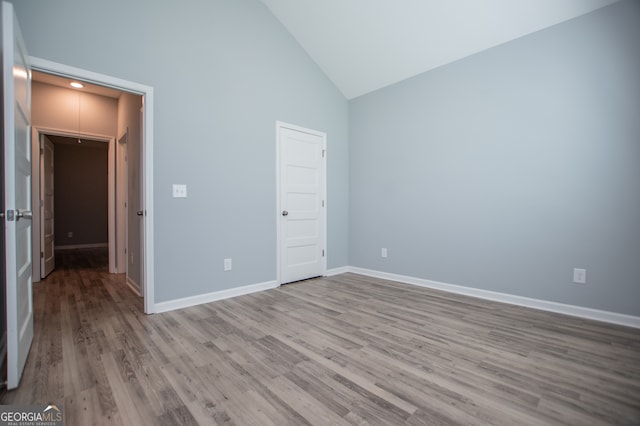 unfurnished bedroom with high vaulted ceiling and wood-type flooring