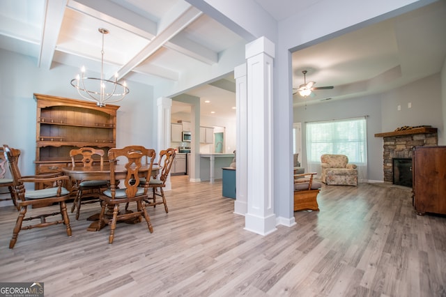 dining area featuring light wood-type flooring, ceiling fan with notable chandelier, decorative columns, and a stone fireplace