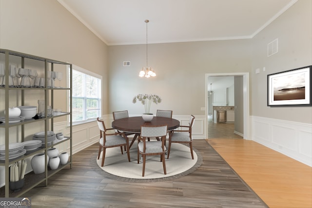 dining room with a towering ceiling, an inviting chandelier, crown molding, and wood-type flooring