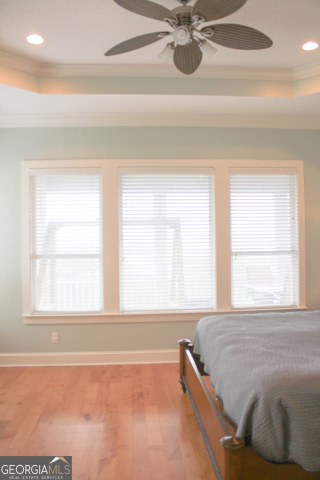 bedroom featuring light hardwood / wood-style flooring, a tray ceiling, ceiling fan, and crown molding