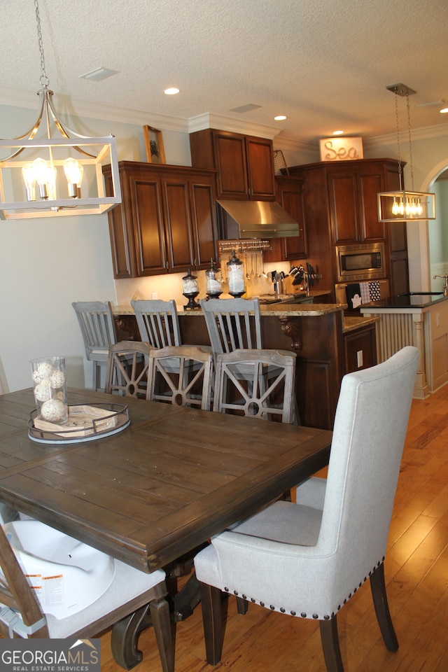 dining room featuring a notable chandelier, light wood-type flooring, a textured ceiling, and ornamental molding