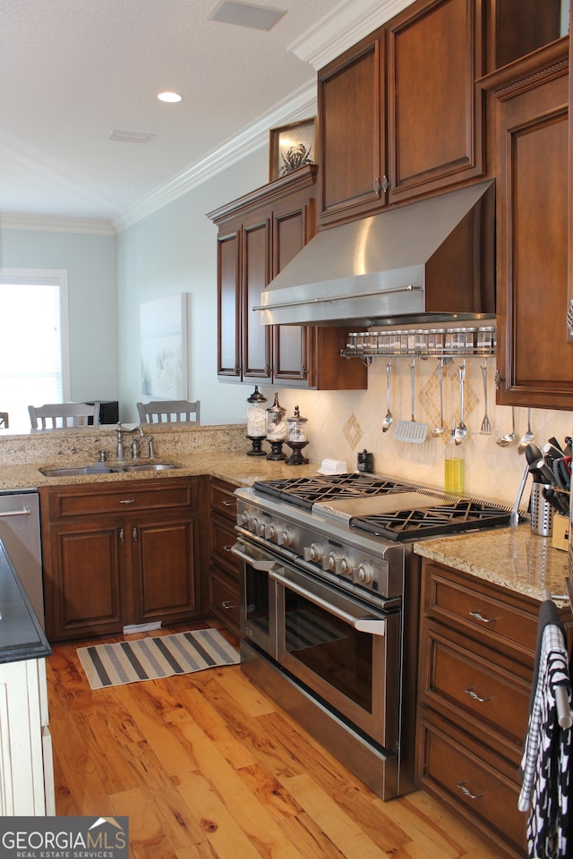 kitchen with appliances with stainless steel finishes, decorative backsplash, light hardwood / wood-style floors, crown molding, and extractor fan