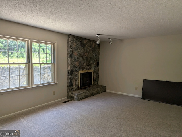 unfurnished living room featuring light carpet, a stone fireplace, a textured ceiling, and track lighting