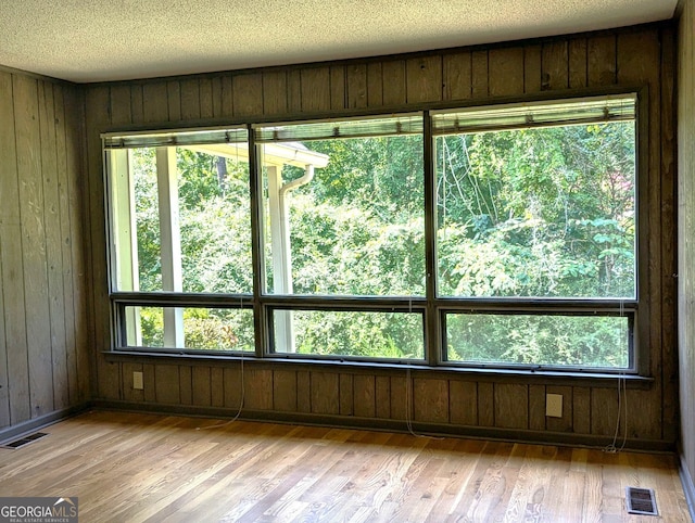 spare room with light hardwood / wood-style floors, wood walls, and a wealth of natural light