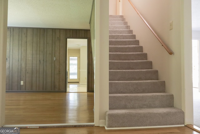 staircase with a textured ceiling, lofted ceiling, wooden walls, and hardwood / wood-style flooring