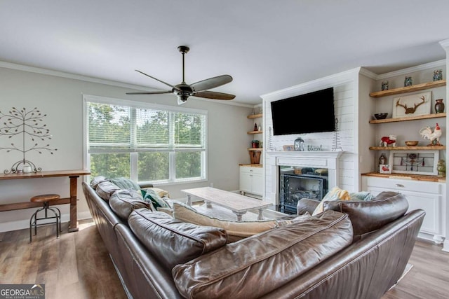 living room with ceiling fan, light hardwood / wood-style flooring, a large fireplace, and ornamental molding