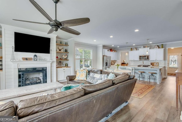 living room with ceiling fan, a fireplace, light hardwood / wood-style floors, and ornamental molding