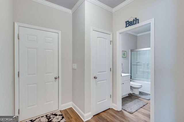 interior space featuring hardwood / wood-style floors, combined bath / shower with glass door, vanity, crown molding, and toilet