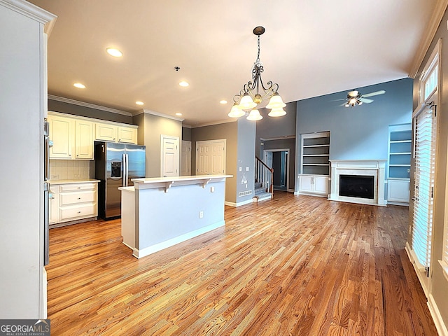 kitchen with light hardwood / wood-style flooring, pendant lighting, stainless steel refrigerator with ice dispenser, ceiling fan with notable chandelier, and a breakfast bar