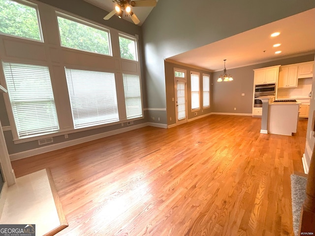 unfurnished living room featuring a towering ceiling, ceiling fan with notable chandelier, and light wood-type flooring