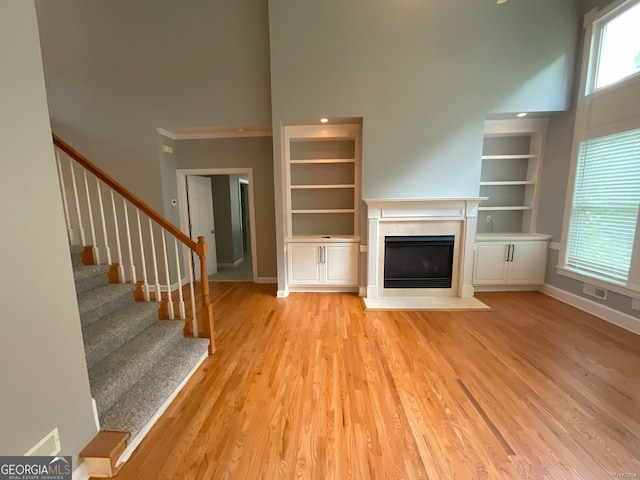 unfurnished living room with light hardwood / wood-style floors, crown molding, a high ceiling, and a premium fireplace