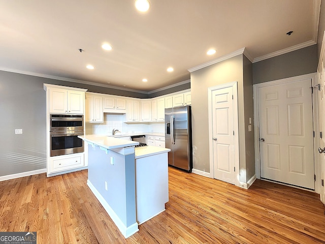 kitchen featuring light hardwood / wood-style flooring, a kitchen island, tasteful backsplash, white cabinetry, and appliances with stainless steel finishes