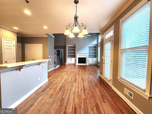 interior space featuring crown molding, hardwood / wood-style floors, an inviting chandelier, and built in features