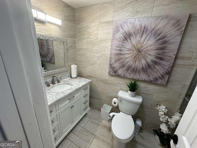 bathroom with tile walls, toilet, vanity, and tile patterned floors