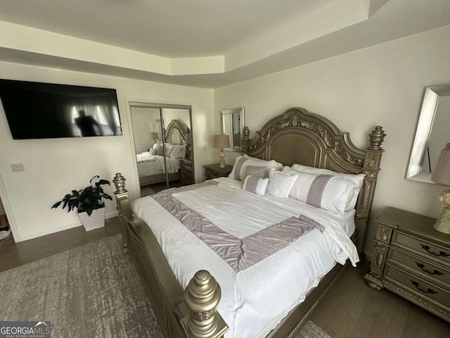 bedroom with dark hardwood / wood-style floors, a closet, and a raised ceiling