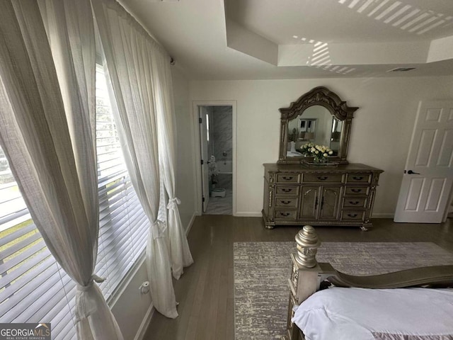 bedroom with multiple windows, dark hardwood / wood-style flooring, connected bathroom, and a tray ceiling