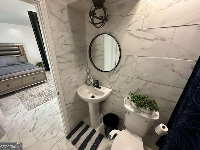 bathroom with toilet, tile patterned floors, and tile walls