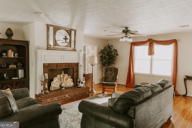 living room with ceiling fan, a brick fireplace, light hardwood / wood-style flooring, and a textured ceiling