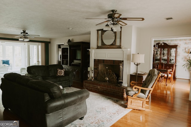 living room with ceiling fan, wood-type flooring, a brick fireplace, and a textured ceiling