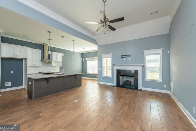 kitchen featuring wall chimney exhaust hood, tasteful backsplash, ceiling fan, a high end fireplace, and a center island with sink