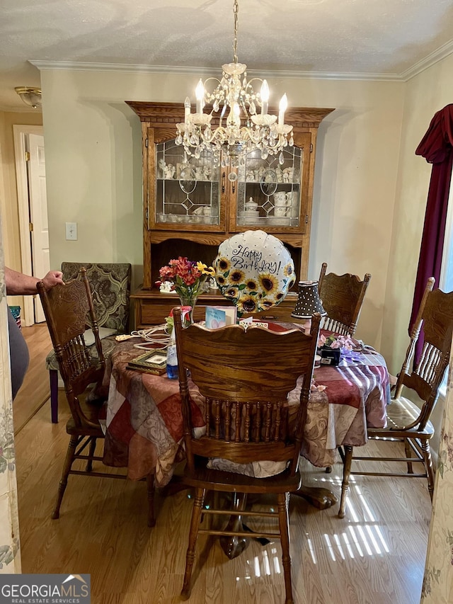 dining space featuring a textured ceiling, a chandelier, ornamental molding, and light hardwood / wood-style flooring