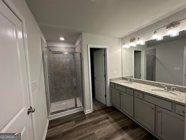 bathroom with hardwood / wood-style flooring, a shower with door, and dual vanity