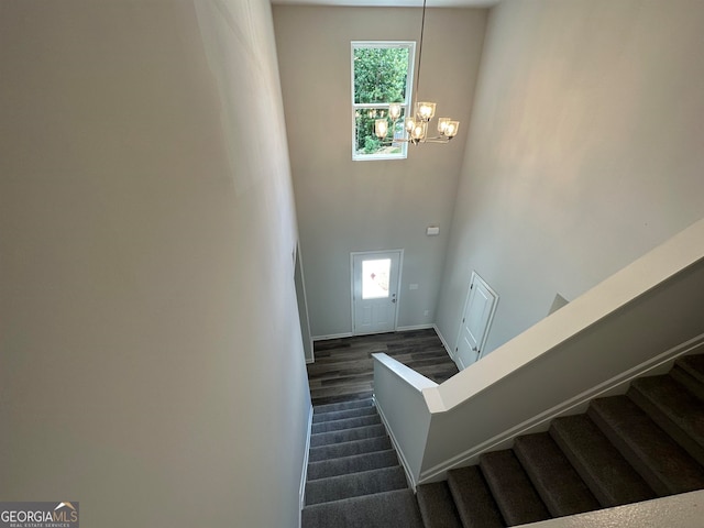 staircase featuring a high ceiling, a notable chandelier, and dark wood-type flooring