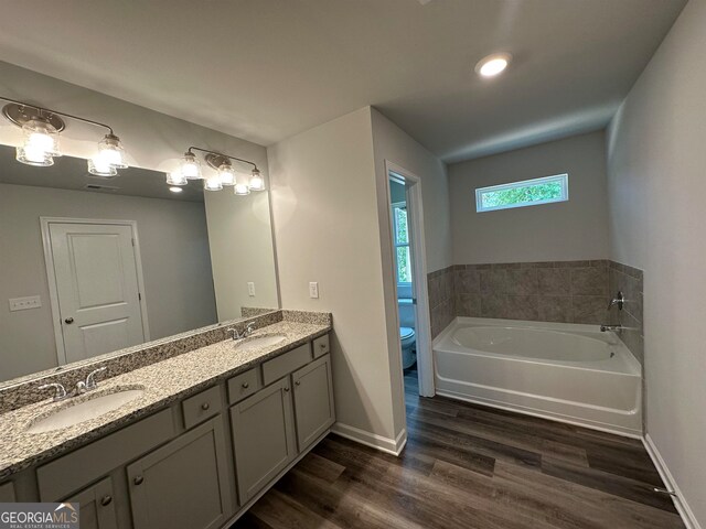 bathroom featuring hardwood / wood-style flooring, toilet, dual bowl vanity, and a tub