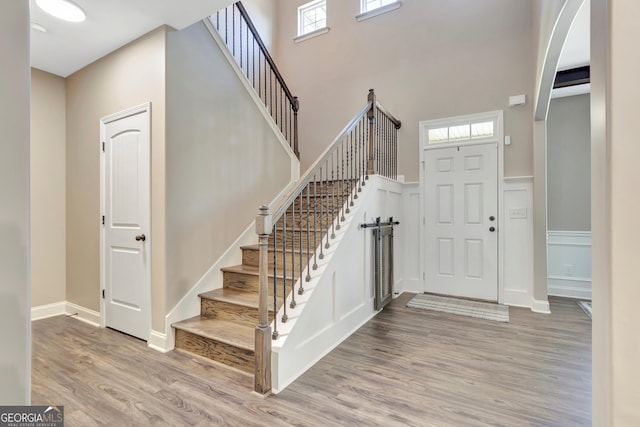 entryway with a wainscoted wall, light wood-style flooring, stairway, a high ceiling, and a decorative wall