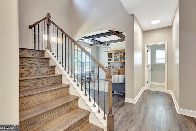 stairs with coffered ceiling, beam ceiling, and wood-type flooring