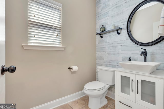 half bath featuring toilet, wood walls, vanity, baseboards, and tile patterned floors