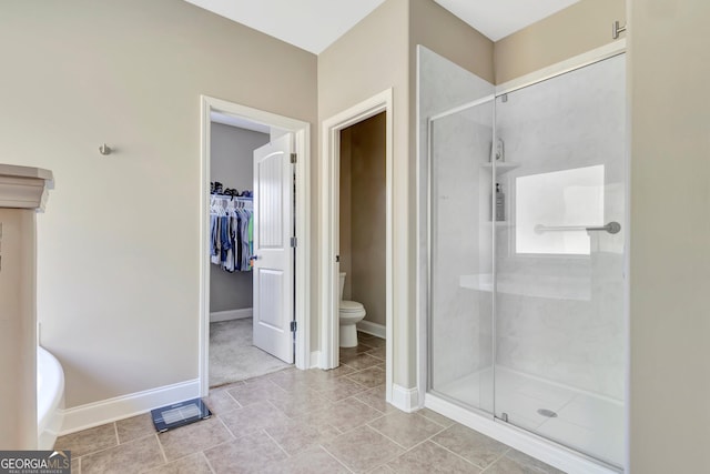 bathroom with a spacious closet, toilet, a stall shower, baseboards, and tile patterned floors