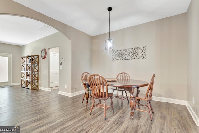 dining area featuring arched walkways, baseboards, and wood finished floors