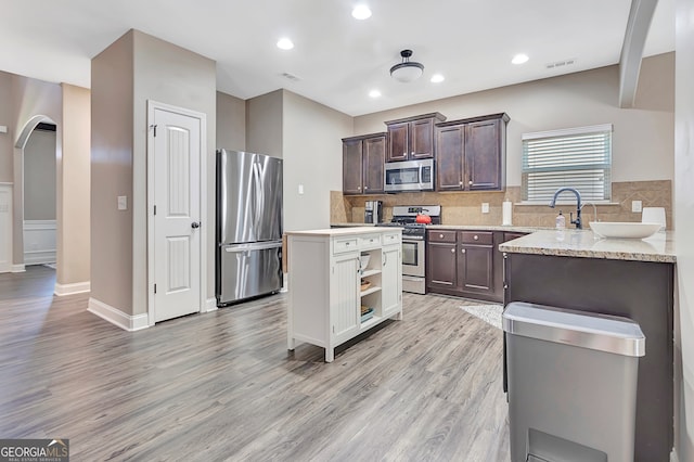 kitchen featuring appliances with stainless steel finishes, dark brown cabinetry, light hardwood / wood-style flooring, and tasteful backsplash